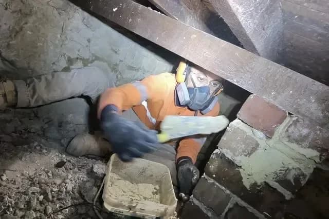A tradesperson working in the subfloor crawl space